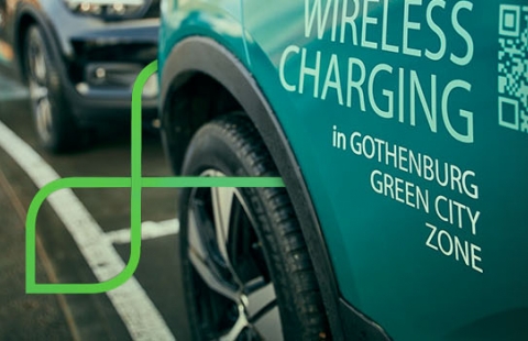 Segue Dé     Close em lateral de carro estacionado sobre marcação em linha branca no solo. Na porta do automóvel lê-se em letras garrafais: 'Wireless Charging'. Logo abaixo, em letras menores, lê-se 'in Gothenburg Green City Zone'. Ao fundo, outro carro do mesmo modelo estacionado.